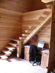 a computer desk under a wooden staircase in a room with wood paneling on the walls