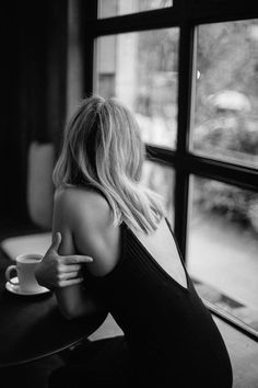 a black and white photo of a woman sitting at a table with a coffee cup