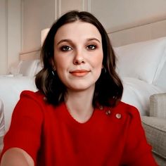 a woman in a red shirt is sitting on a couch and looking at the camera