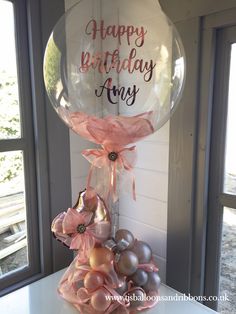 a birthday cake with balloons and flowers on it's stand in front of a window