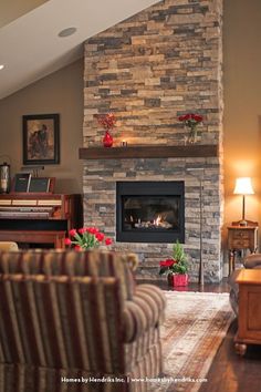 a living room with a stone fireplace and piano in the corner, surrounded by chairs