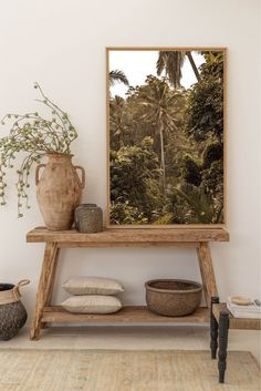 a wooden table topped with a vase filled with flowers next to a painting on the wall