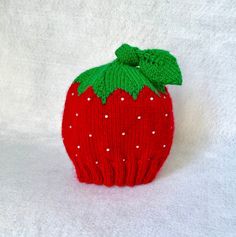 a red knitted strawberry with green leaves on it's side sitting on a white surface