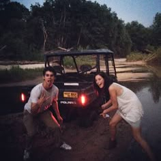 two people standing in front of a jeep at night with the headlights on and one person leaning over