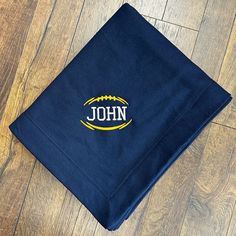 a blue towel with the name john on it sitting on a wooden floor next to a pair of scissors