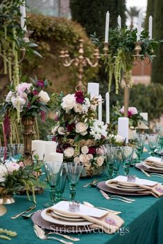 the table is set with green linens and gold place settings, white flowers, greenery, candles, and napkins