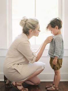 a woman kneeling down next to a little boy on top of a hard wood floor