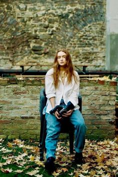 a woman sitting on top of a chair in front of a brick wall holding a camera