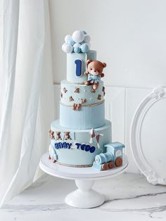 a three tiered blue cake with teddy bears on top and train decorations around the edges