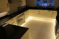 a kitchen with white cabinets, black counter tops and lights on the floor in front of windows