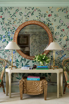 a table with two chairs and a mirror on it in front of a floral wallpaper