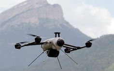 a small white and black propellered airplane flying in the air with mountains in the background