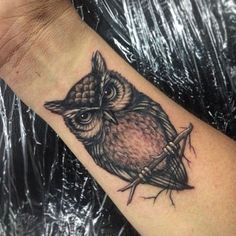 an owl tattoo on the wrist is shown in black and grey ink, with a small bird