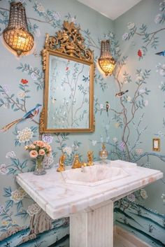 a bathroom with blue and gold wallpaper, a marble pedestal sink and two hanging lights