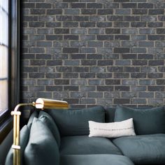 a blue couch sitting in front of a brick wall next to a window with a lamp on it