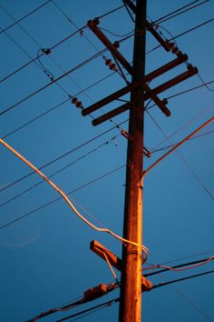 an electric pole with many wires and telephone poles in the foreground, against a blue sky