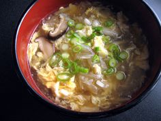 a red bowl filled with soup on top of a black counter next to a spoon