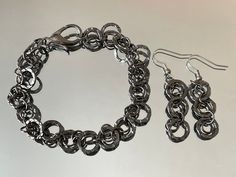 Gunmetal grey chain bracelet and earrings set is retro-styled 80s, and features a geometric design of handcrafted chain-link (chainmail/chain maille) circles. Shiny gray steel circles have a hammered texture, with smaller circles layered and linking for a light chainmail weave.  Perfect with black, red, charcoal gray, and any jewel-tone color (think burgundy, emerald, teal, or amethyst!) this chunky chain link bracelet and earrings set is versatile, classy, lightweight and fun!  Looks great alon Chain Maille, Circle Bracelet, Jewel Tone Colors, Punk Jewelry, Gunmetal Grey, Jewelry Card, Steel Jewelry, Jewel Tones, Retro Stil