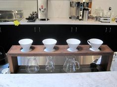 four coffee cups are lined up on a counter in a kitchen with stainless steel appliances