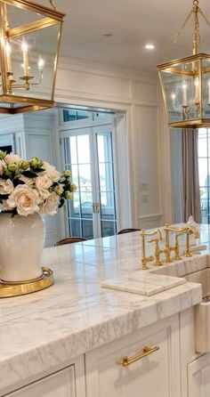 a large kitchen with marble counter tops and gold accents on the cabinets, along with two chandeliers hanging from the ceiling