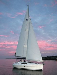 a sailboat is sailing in the water at sunset with pink and blue clouds behind it