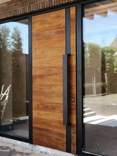 a wooden door with black frame and glass on the side of a brick building in front of trees