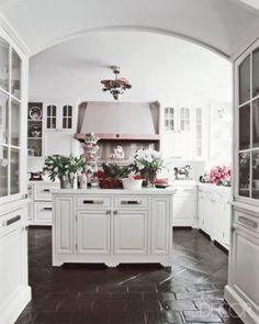 a kitchen with white cabinets and lots of flowers on the counter top in front of an arched doorway