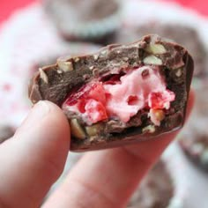 a hand holding up a chocolate cookie with ice cream and nuts on the inside, in front of other cookies