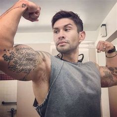 a man is flexing his muscles in the bathroom with tattoos on his arms and shoulder