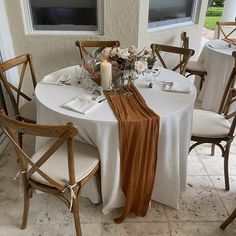 the table is set with white linens and flowers on it, along with candles