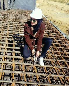 a woman kneeling on top of a pile of metal grates in the middle of a construction site