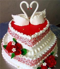 two swans on top of a wedding cake with red and white flowers in the middle