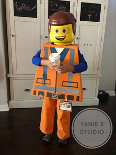 a young boy dressed up as a lego character holding a cup of coffee and wearing an orange vest