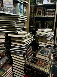 many books are stacked on top of each other in a room full of bookshelves