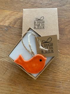 an orange bird ornament in a box on a wooden table with a tag