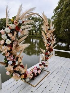 an arch made out of dried flowers and pamodia on a dock next to a lake