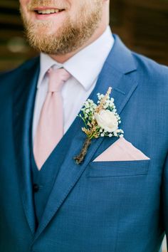 a man in a blue suit with a pink tie and flower boutonniere