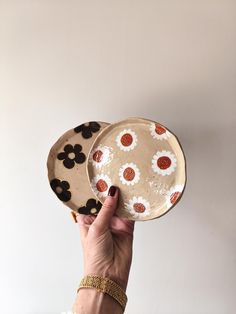 a person holding up a plate with flowers on it in front of a white wall