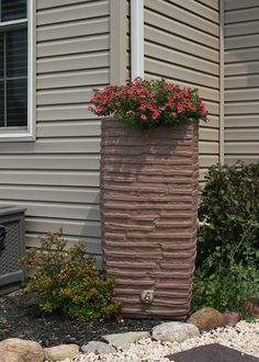 a planter with flowers in it sitting on the side of a house next to rocks