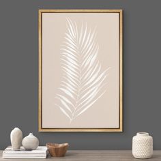 a white vase sitting on top of a wooden table next to a framed plant in front of a gray wall