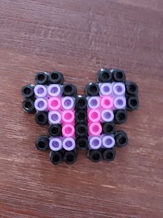 two black and pink beads are sitting on a wooden surface, one is shaped like a butterfly