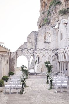 an outdoor ceremony setup with white chairs and greenery on the ground in front of a stone building