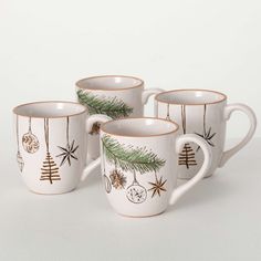 three coffee mugs decorated with christmas ornaments and pine branches, on a white background