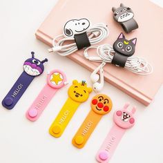 four different colored cartoon key chains on top of a pink book with earphones attached to them