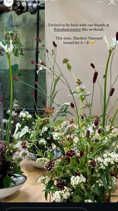 a table topped with vases filled with flowers and greenery next to a sign