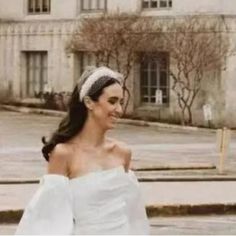 a woman wearing a white dress and headband walking down the street in front of a building