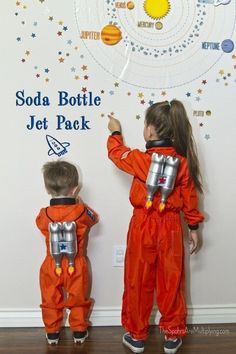 two little kids dressed in space suits standing next to each other and writing on the wall