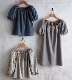 three blouses hanging up against a wall, one in grey and the other in blue