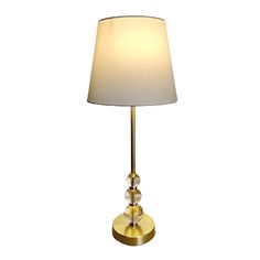 a table lamp with a white shade on it's side and a gold base