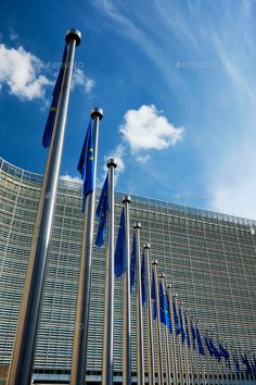 many flags are flying in front of a large building with glass walls and blue sky